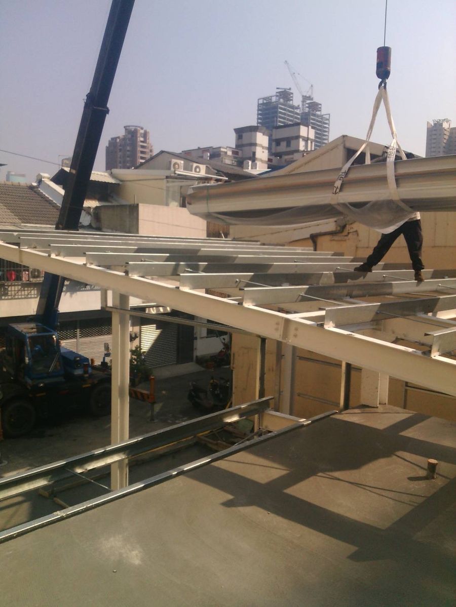 吊車將浪板吊上屋頂,師傅於鋼架上接料